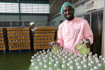 Wall Mural - African male factory worker picking up green juice bottle or basil seed drink for checking quality in beverage factory