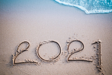 Happy New Year 2021 concept, 2021 number lettering on the sea beach, wave and golden light of sunset.