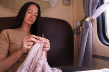 Middle Aged Woman Sitting On Sofa In Compartment  Of Train And Knitting Clothe. 