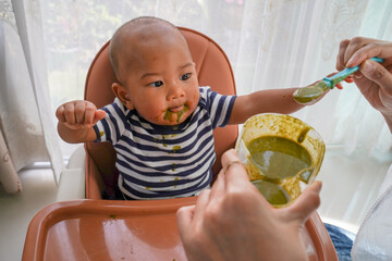 An asian kid boy in high chair or feeding table eating healthy food. Concept of child food, family care and child eats food.