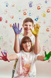 © Svitlana - Happy kids, disabled boy and girl with Down syndrome smiling at camera, showing their hands painted in colorful paints for hand prints on the wall