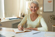 © Anatoliy Karlyuk - Portrait of happy confident middle aged woman freelancer working from home office, sitting at table with portable computer, holding pen, handwriting in journal. Age, job and remote work concept