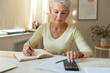 © Anatoliy Karlyuk - Concentrated middle aged woman with short hair calculating income and expenses, paying domestic bills, writing down in journal, sitting at table. People, finance, economy and paperwork concept