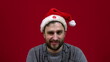 © Sergei Puzankov - The man is sitting and a Christmas hat is dancing on his head. Santa's bearded helper on red background