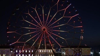 Wall Mural - Ferris wheel with glowing multicolored lights against the night sky.