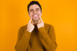 © Jihan - Strong healthy straight white teeth. Close up portrait of happy Young handsome Caucasian man wearing yellow sweater against orange wall with beaming smile pointing on perfect clear white teeth.