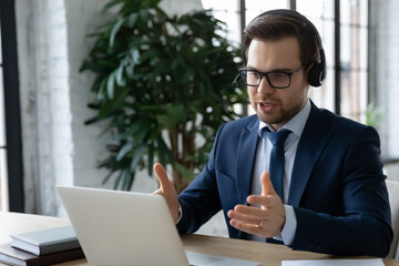 Wall Mural - Close up focused employee wearing glasses and headset consulting client, using laptop, confident businessman looking at laptop screen, making video call to business partner, chatting online