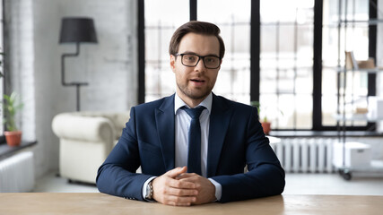 Wall Mural - head shot confident businessman wearing suit and glasses speaking looking at camera, sitting at work