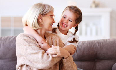 Wall Mural - Happy grandmother and granddaughter hugging on sofa.