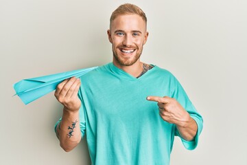 Wall Mural - Young caucasian man holding paper airplane smiling happy pointing with hand and finger