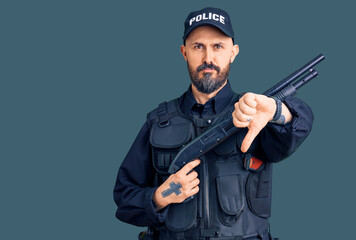 Poster - Young handsome man wearing police uniform holding shotgun with angry face, negative sign showing dislike with thumbs down, rejection concept