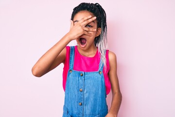 Poster - Young african american girl child with braids wearing casual clothes over pink background peeking in shock covering face and eyes with hand, looking through fingers with embarrassed expression.