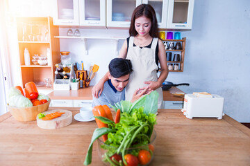 Cooking healthy food. Happy young couple cooking together in the kitchen while man touching abdomen of his pregnant wife.