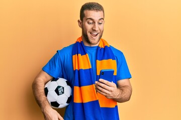 Sticker - Young caucasian man holding football ball looking at smartphone celebrating crazy and amazed for success with open eyes screaming excited.