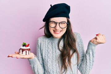 Sticker - Young beautiful caucasian girl wearing french beret holding cake screaming proud, celebrating victory and success very excited with raised arm