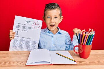 Wall Mural - Adorable caucasian kid holding passed test sitting on the table pointing thumb up to the side smiling happy with open mouth