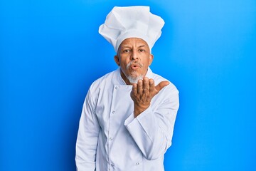 Poster - Middle age grey-haired man wearing professional cook uniform and hat looking at the camera blowing a kiss with hand on air being lovely and sexy. love expression.