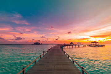 Sunset on Maldives island, luxury water villas resort and wooden pier. Beautiful sky and clouds and beach background for summer vacation holiday and travel concept. Paradise sunset sunrise landscape