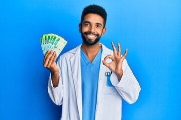 Wall Mural - Handsome hispanic man with beard wearing medical uniform holding 200 russian ruble doing ok sign with fingers, smiling friendly gesturing excellent symbol