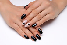 Black, beige manicure with black hearts on short oval nails close-up on a white background