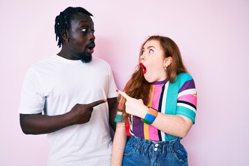 Wall Mural - Interracial couple wearing casual clothes surprised pointing with finger to the side, open mouth amazed expression.