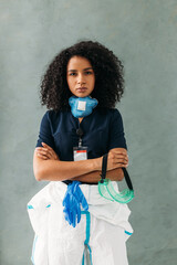 Wall Mural - Young serious nurse standing at wall with arms crossed wearing and holding protective accessories