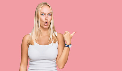 Sticker - Young blonde girl wearing casual style with sleeveless shirt surprised pointing with hand finger to the side, open mouth amazed expression.