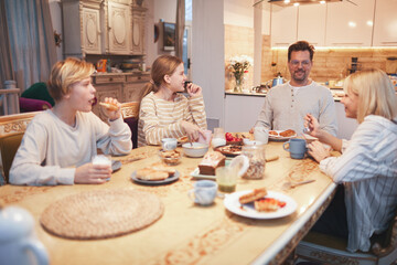 Wide angle portrait of big happy family enjoying breakfast together sitting at table in kitchen , focus on smiling father and three kids, copy space