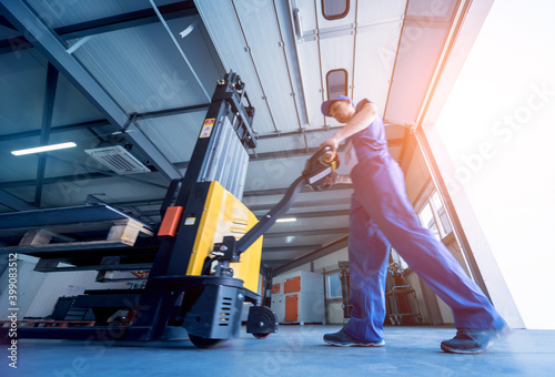 Obraz na plátně A worker in a warehouse uses a hand pallet stacker to transport pallets