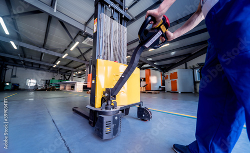 Fotografie, Obraz A worker in a warehouse uses a hand pallet stacker to transport pallets