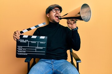 Sticker - Handsome man with tattoos holding video film clapboard and louder angry and mad screaming frustrated and furious, shouting with anger looking up.