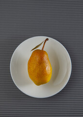 Ripe pear fruit lies on a white plate on a gray background.