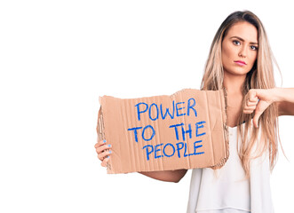 Sticker - Young beautiful blonde woman holding power to the people cardboard banner with angry face, negative sign showing dislike with thumbs down, rejection concept