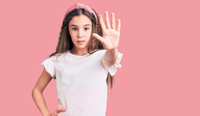 Cute hispanic child girl wearing casual white tshirt doing stop sing with palm of the hand. warning expression with negative and serious gesture on the face.