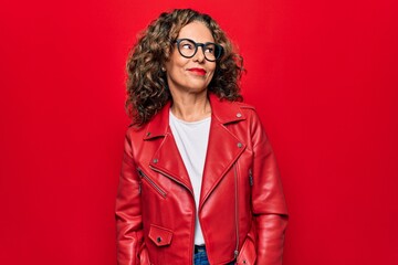 Middle age beautiful woman wearing casual red jacket and glasses over isolated background looking to side, relax profile pose with natural face and confident smile.