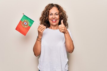 Sticker - Middle age beautiful patriotic woman holding portuguese flag over isolated white background smiling happy and positive, thumb up doing excellent and approval sign