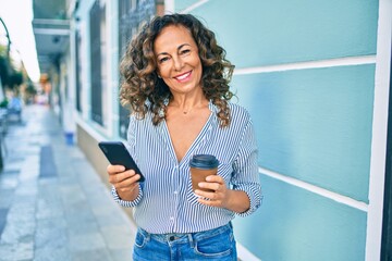 Canvas Print - Middle age hispanic woman using smartphone and drinking take away coffee at the city.