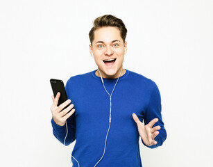 young handsome man on white studio background listening to music on earphones