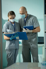 Poster - Clinicians in uniform, protective masks and gloves discussing medical documents
