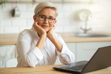 Wall Mural - beautiful adult woman in glasses at the table with laptop at home