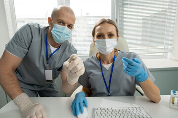 Poster - Two contemporary clinicians in protective workwear looking at computer screen