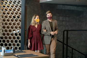 Poster - Young couple in protective masks and smart casualwear entering restaurant
