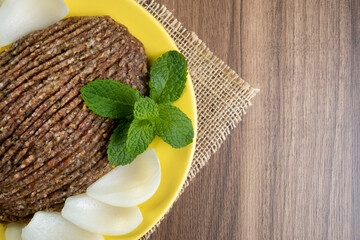 raw quibe with sliced onion and a sprig of mint