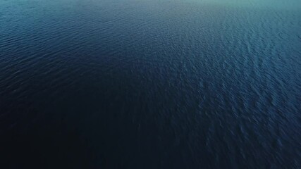 flying backwards above dark blue water surface. aerial view during dusk