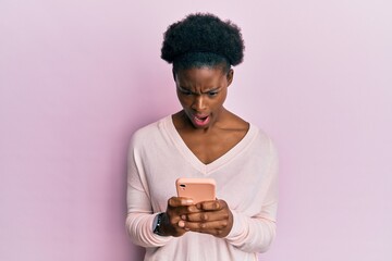 Canvas Print - Young african american girl using smartphone angry and mad screaming frustrated and furious, shouting with anger. rage and aggressive concept.