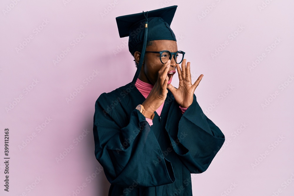 Young african american girl wearing graduation cap and ceremony robe shouting angry out loud with hands over mouth - obrazy, fototapety, plakaty 