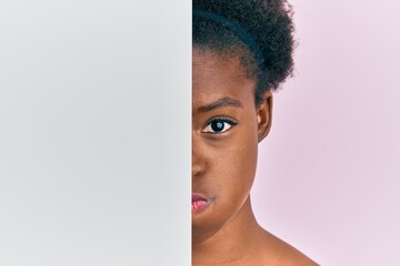 Poster - Young african american girl holding blank empty banner over half face puffing cheeks with funny face. mouth inflated with air, catching air.