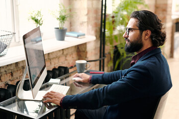 Poster - Serious young bearded broker or economist in suit sitting in front of computer