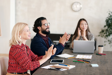Poster - Happy intercultural professionals clapping their hands while sitting by table