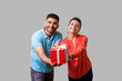 © khosrork - Please take your present! Young generous couple giving gift box to camera, looking with toothy smile, sharing present on holidays, charity concept. isolated on gray background, indoor studio shot
